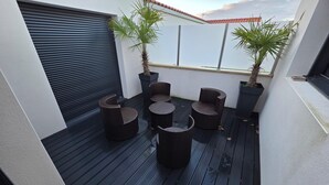 Una terraza en la azotea con piso negro, una puerta de garaje cerrada y varios sillones y mesas de mimbre.