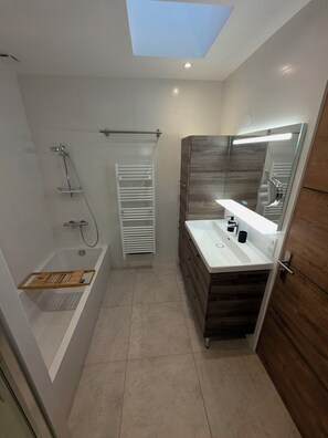 Un bagno moderno con un lucernario, una vasca da bagno con un vassoio di legno, una doccia con box in vetro e un mobile lavabo con specchio.