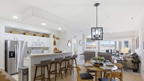 A modern kitchen with white cabinets, a stainless steel refrigerator, and a dining area with wooden chairs and a table. - 2B 2B | Lake View | Seasonal Pool | Hot Tub |Grill (Lake Ozark)