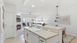 A modern kitchen with white cabinetry, a large island, and a dining area with a fireplace. - 2B 2B | Lake View | Seasonal Pool | Hot Tub |Grill (Lake Ozark)
