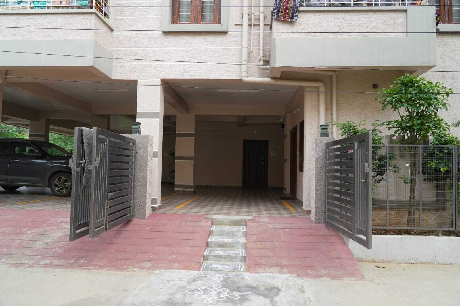 Entrada de un edificio con zona de estacionamiento techada, una escalera y un camino de acceso con portón.