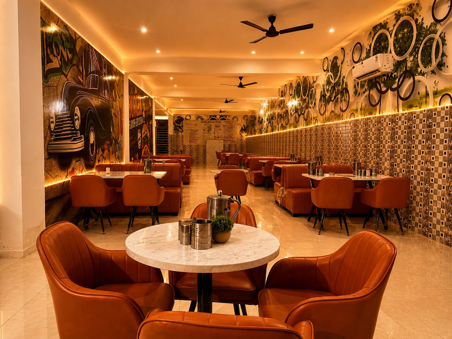 A restaurant interior with round tables and orange chairs, ceiling fans, and decorative wall art.