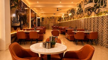 A restaurant interior with round tables and orange chairs, ceiling fans, and decorative wall art.