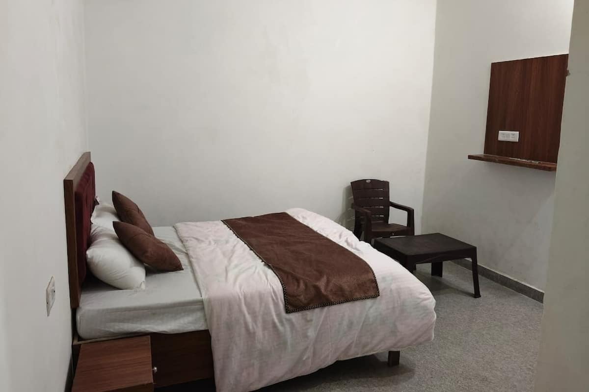 A bedroom with a bed, a chair, a small table, and a wooden shelf.