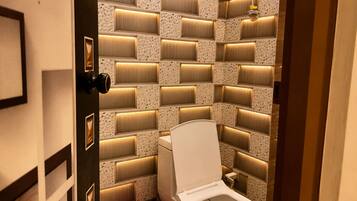 A modern bathroom with a unique tiled wall design, a toilet, and a red bucket.