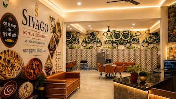 A hotel lobby with a reception desk, seating area, and a wall decorated with circular patterns and plants.