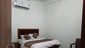 Een slaapkamer met een bed, een houten nachtkastje, een stoel en een wandairconditioner.