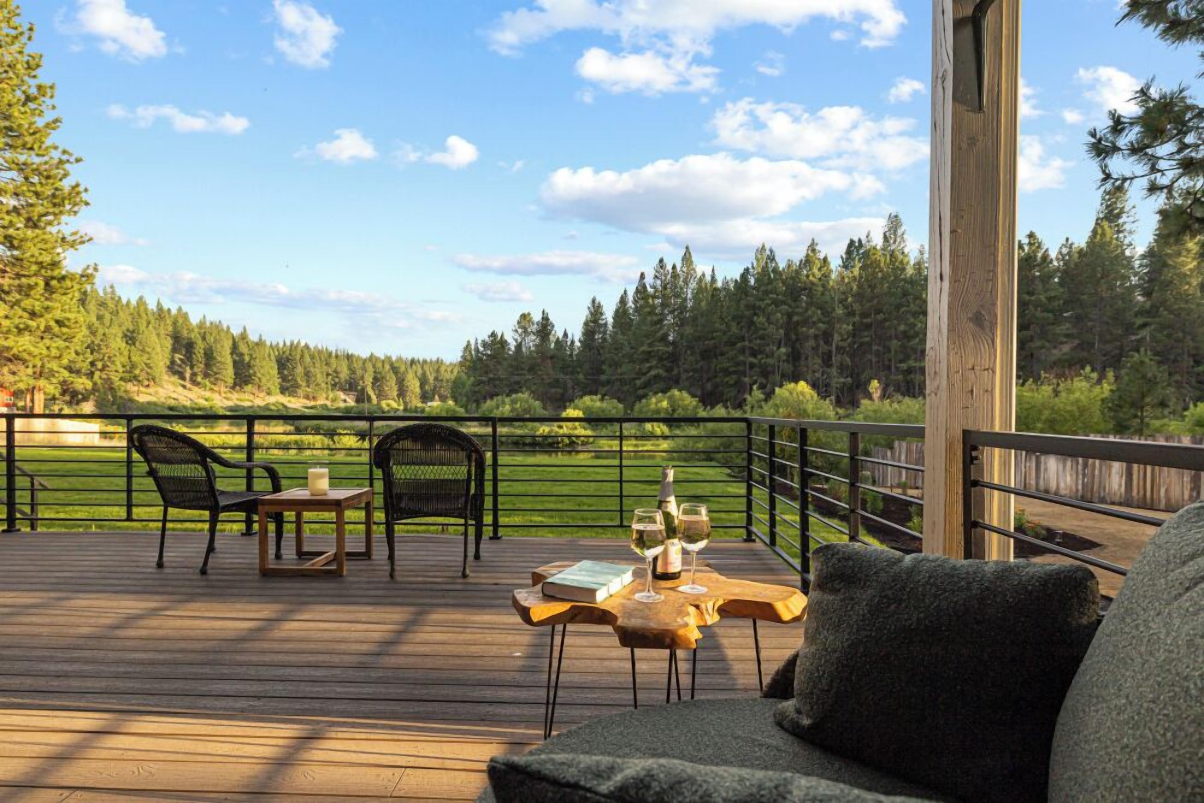 A wooden deck with outdoor furniture, including a table and chairs, overlooking a forested area.