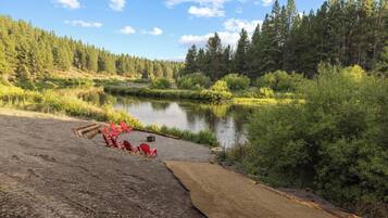 A natural landscape with a lake, forest, and a sandy area with red chairs and a fire pit.