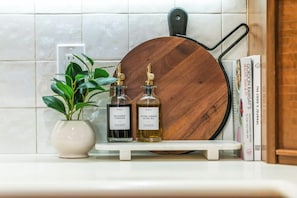 A kitchen counter with a potted plant, two bottles of balsamic vinegar and extra virgin olive oil, a wooden cutting board, and a Gordon Ramsay book.