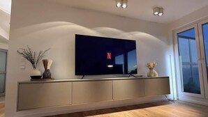 Una sala de estar moderna con un televisor de pantalla plana montado en la pared, suelo de madera y un ventanal grande.