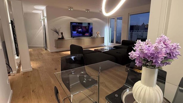 Una sala moderna con una mesa de comedor de vidrio, sofás negros y un televisor de pantalla plana.