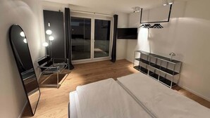 Una habitación de hotel moderna con una cama, un espejo, una silla, un armario y un ventanal corredero que da a un balcón.