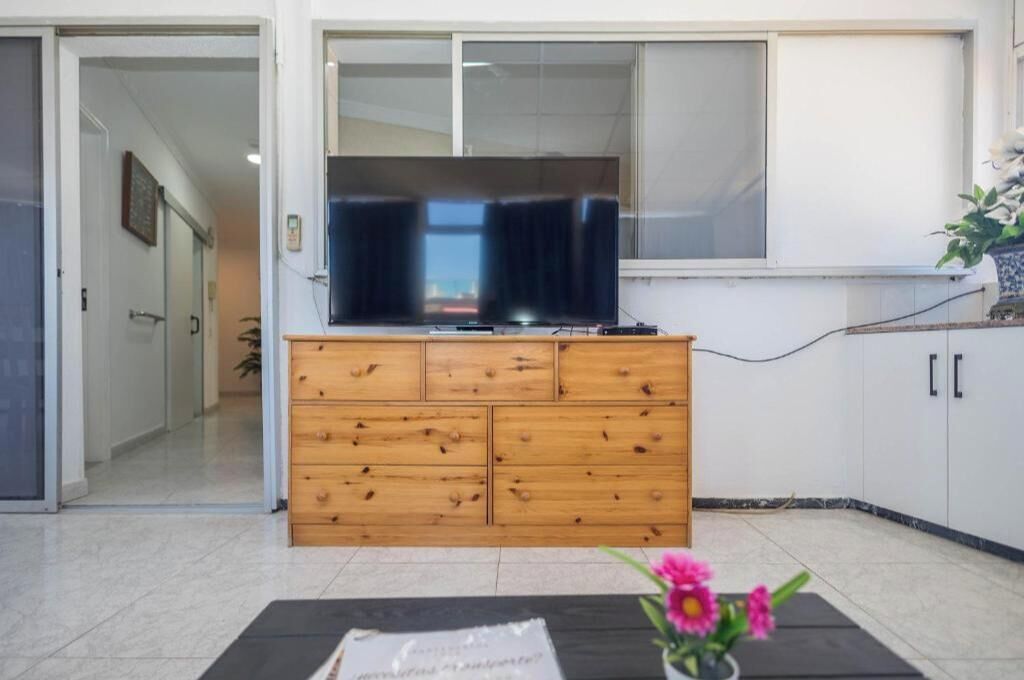 A living room with a wooden cabinet, a flat-screen TV, and a small table with a vase of flowers.