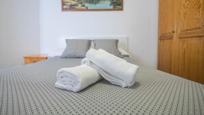 A neatly made bed with rolled white towels, a wooden wardrobe, and a painting on the wall. - 3 bedroom apartment in Arguineguín - Comfort and sun next to the beach (Arguineguín)