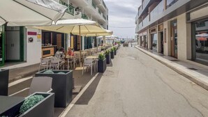 A street with outdoor seating, a building with balconies, and a clear sky. - 3 bedroom apartment in Arguineguín - Comfort and sun next to the beach (Arguineguín)