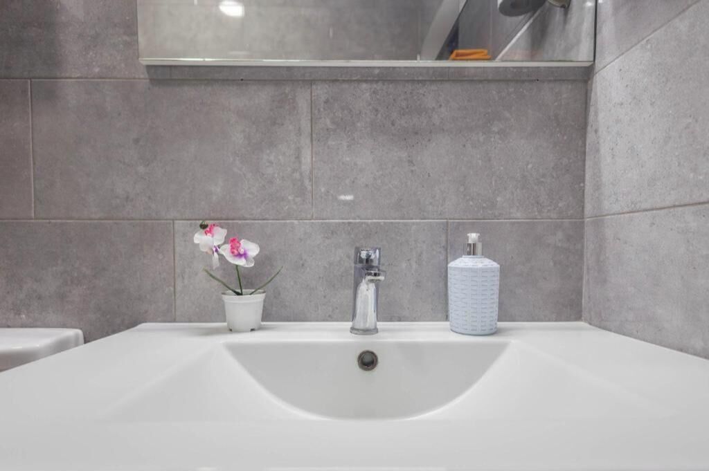 A bathroom with a white sink, a potted orchid, and a soap dispenser.