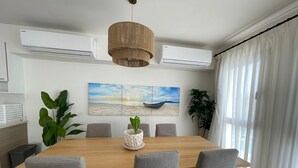 A dining area with a wooden table, grey chairs, a hanging light fixture, and a beach-themed painting on the wall. - Penthouse 4 Bedrooms Marina2-14LR-305 (El Alamein)
