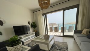 A modern living room with a flat-screen TV, a sofa, a coffee table, and a balcony with a view of the sea. - Penthouse 4 Bedrooms Marina2-14LR-305 (El Alamein)