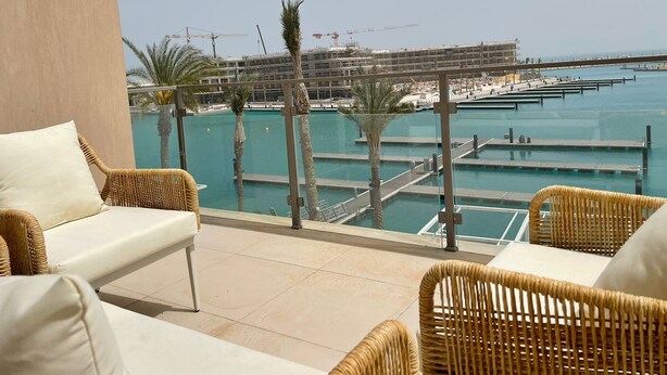 A balcony with wicker furniture, a pool, and a view of a marina with construction. - Penthouse 4 Bedrooms Marina2-14LR-305 (El Alamein)