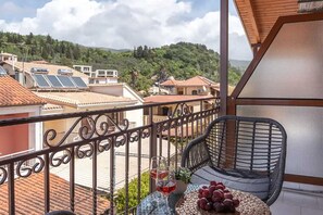 A balcony with a chair, a table with a glass of red wine and grapes, and solar panels on neighboring buildings. - Esperides Erithia-seaside Syvota Mountain View Gem (Igoumenitsa)