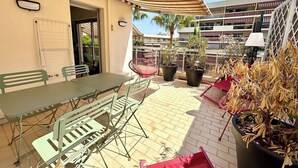 Un patio exterior con mesa y sillas, plantas en macetas y un toldo a rayas.
