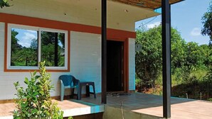 A covered outdoor area with a window, a door, and a small table with a chair. - Alphonso (Shoolagiri)