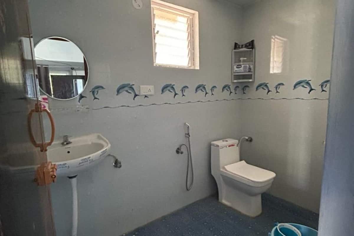 A small bathroom with a sink, toilet, and shower. There is a window and a mirror on the wall.