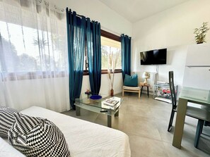 Een woonkamer met een bank, een glazen salontafel, een televisie en een eethoek met een stoel en tafel.
