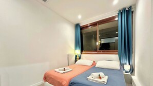 Un lit double avec deux oreillers, une table de chevet avec une lampe, une fenêtre avec des rideaux et un radiateur.