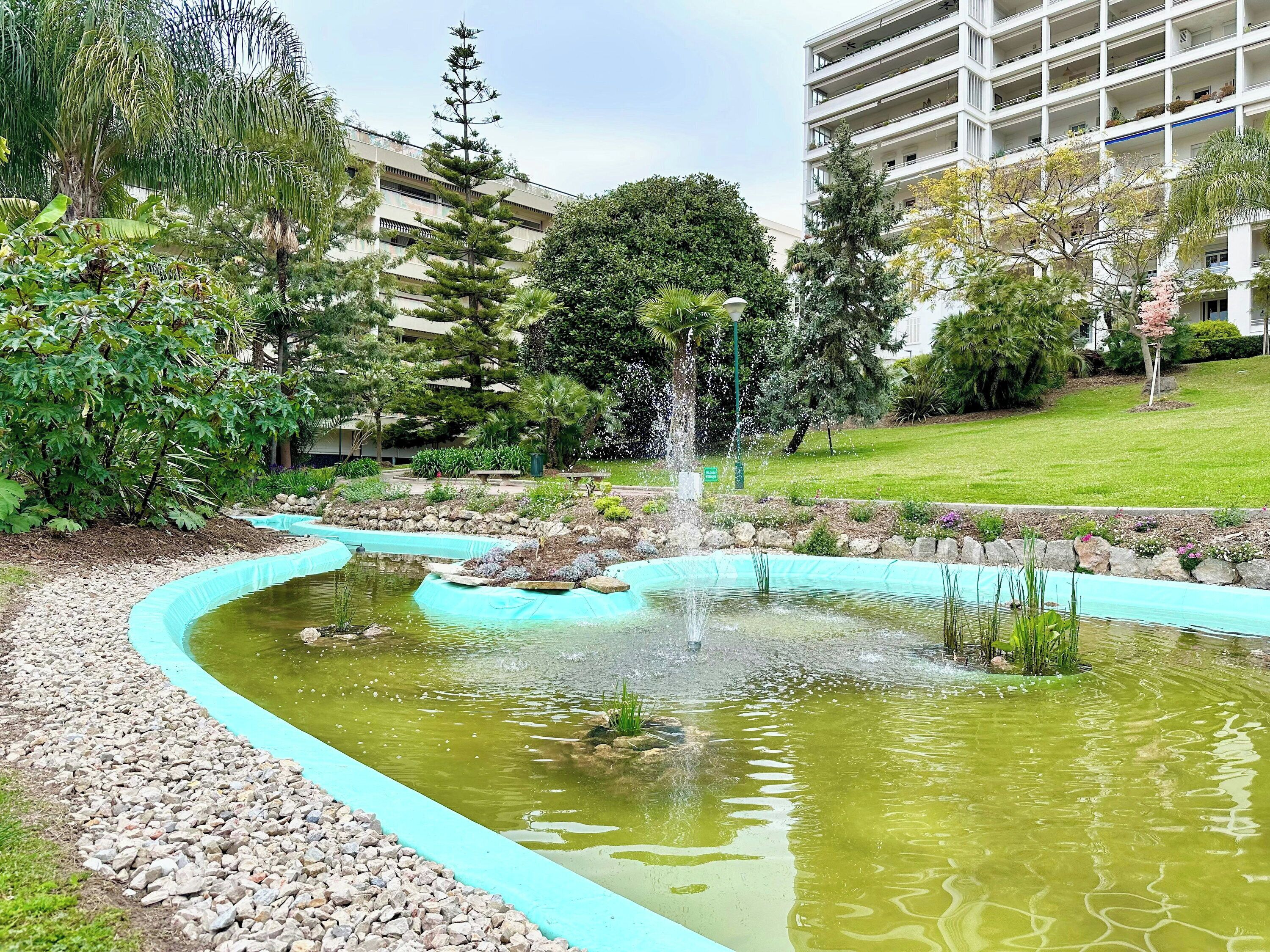 A landscaped garden with a pond, a fountain, and surrounding greenery.