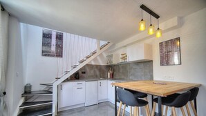 A modern kitchen with a wooden dining table, black chairs, a staircase, and pendant lights. - App. Suzette Duplex - 500m FROM THE BEACH (Cannes)