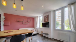 A modern room with a wooden dining table, black chairs, a sofa, a TV mounted on the wall, and a window with curtains. - App. Suzette Duplex - 500m FROM THE BEACH (Cannes)