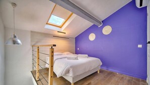 Ein Zimmer mit einem Bett, einem Oberlicht, Holzboden und einer violetten Wand.