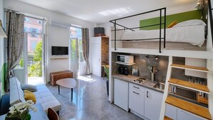 Un studio compact comprenant un coin cuisine, un espace repas, un canapé, une télévision et une fenêtre avec des rideaux.