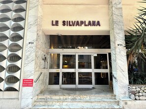 La entrada al hotel Le Silvaplana con escalones de mármol, puerta de vidrio y un letrero que indica zona sin estacionamiento en frente.