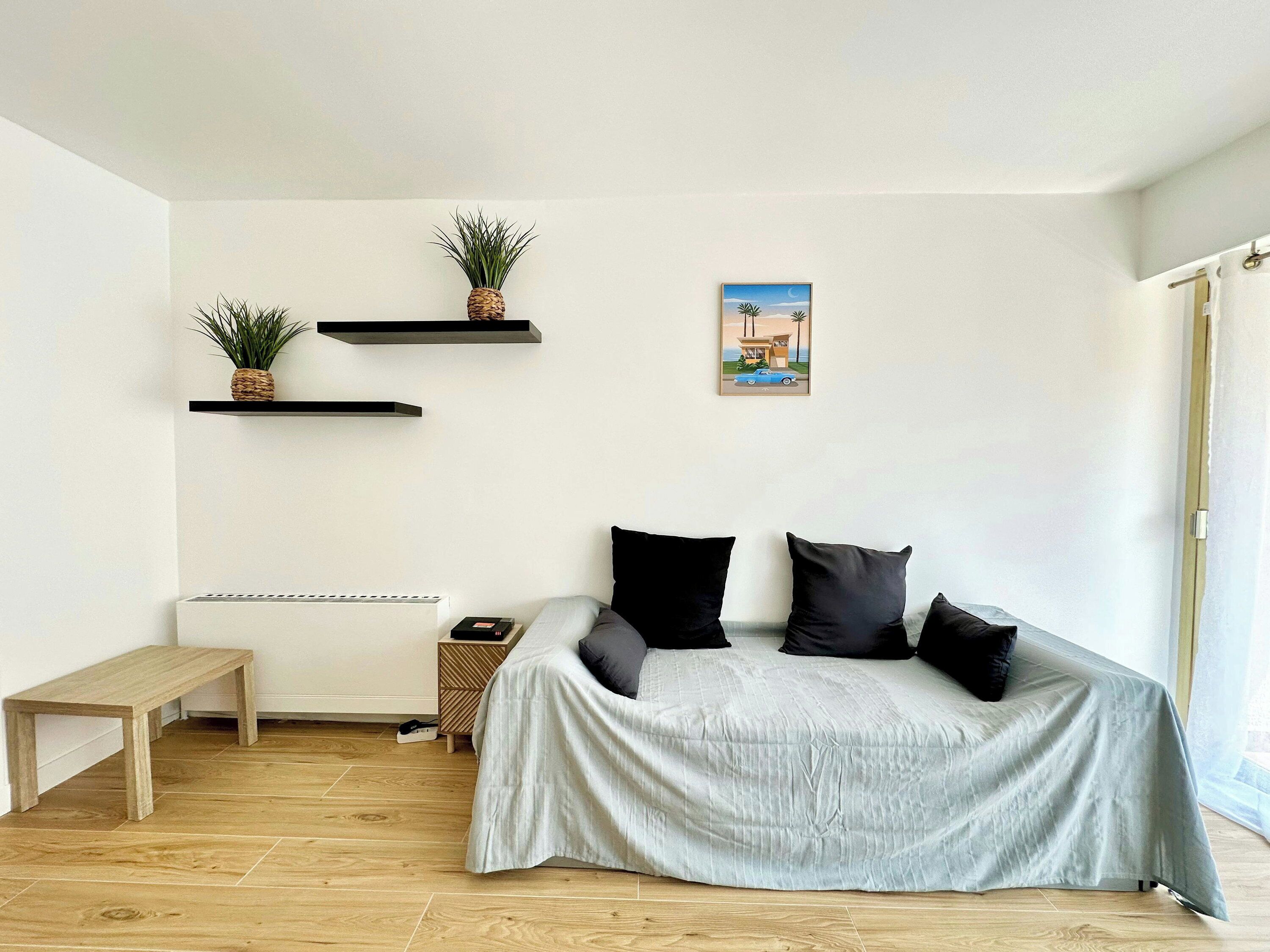 A room with a bed, a bench, and two wall-mounted shelves with plants.