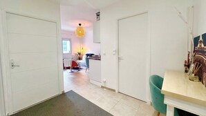 Een gang die uitkomt in een woonruimte met een eettafel, stoelen en een kroonluchter.