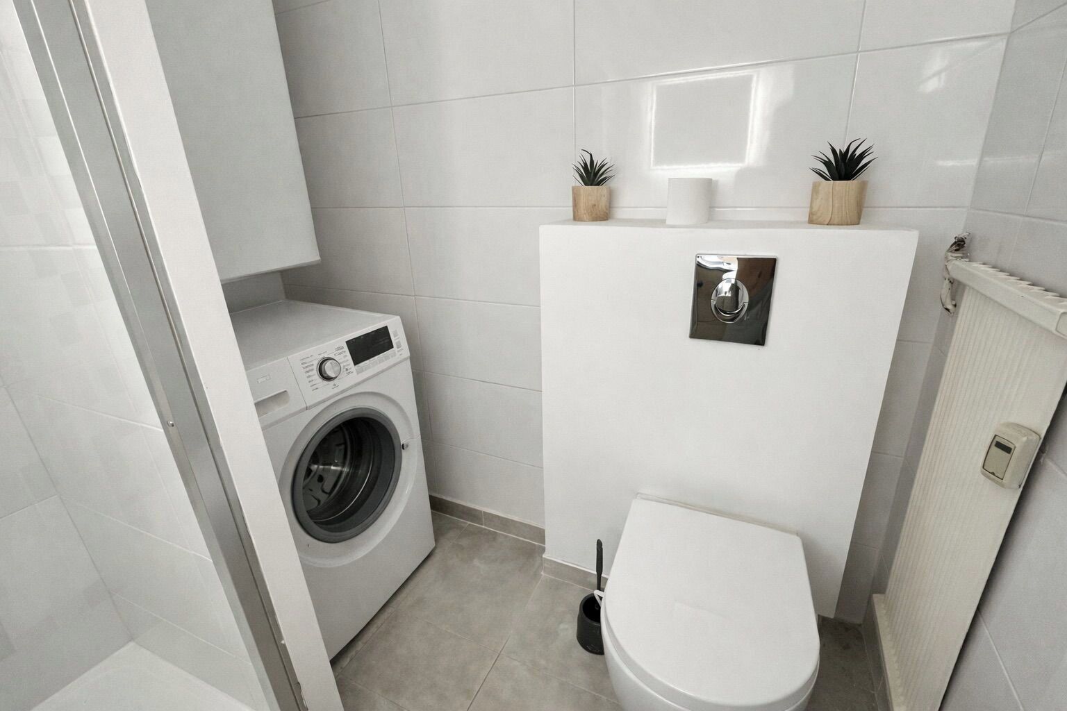 Un bagno compatto con lavatrice, toilette e un piccolo ripiano con piante.