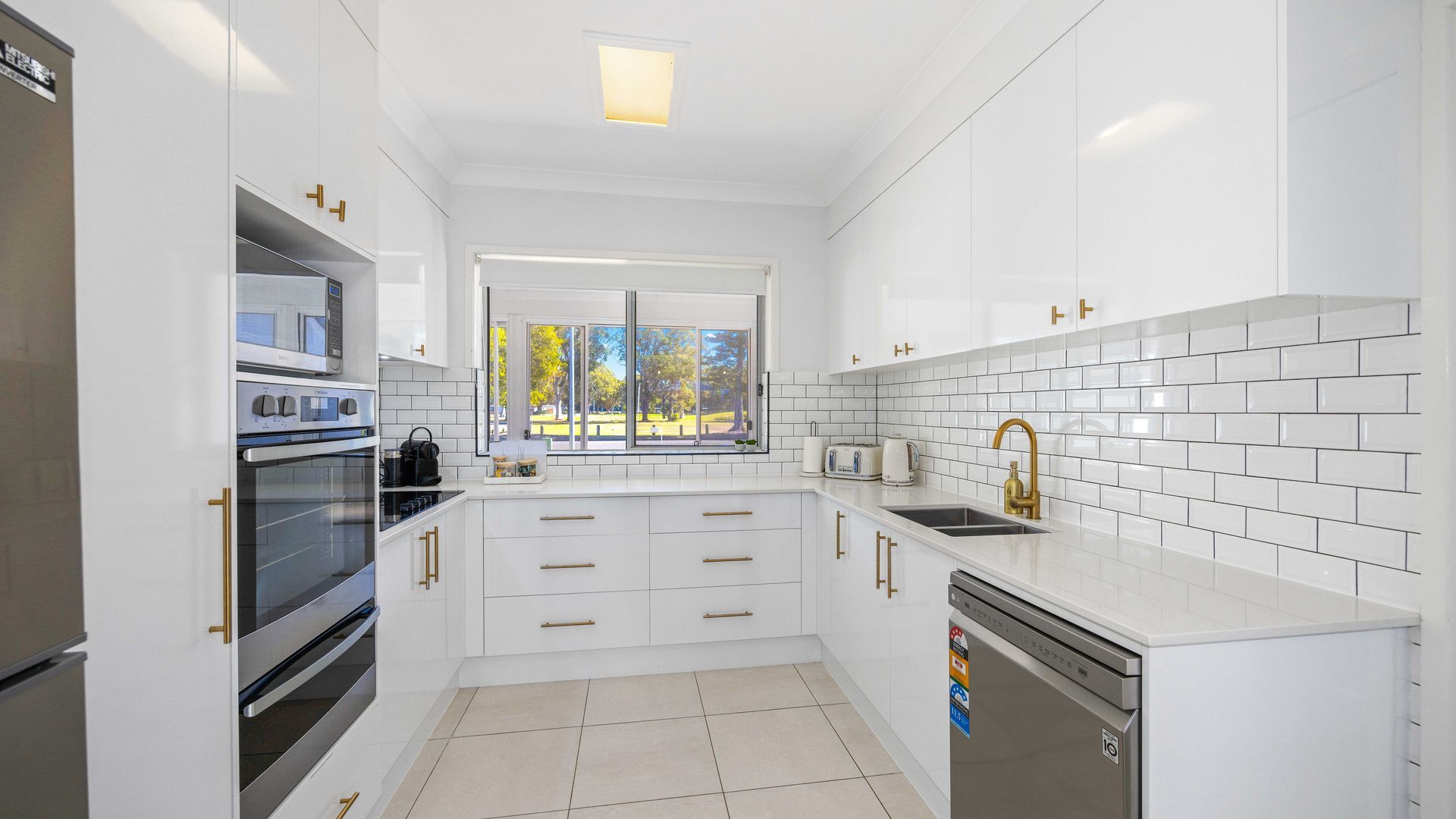 A modern kitchen with white cabinetry, a built-in oven, a dishwasher, and a window with a view of the outdoors.