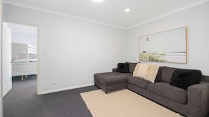A modern living room with a grey sectional sofa, a large mirror, and a painting of a beach scene. - Hibbard Waterfront Escape (Port Macquarie)