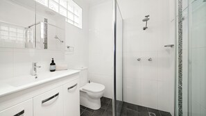 Ein modernes Badezimmer mit einem weißen Waschtisch, einer Toilette, einer Dusche mit Glastür und einem Spiegel mit dekorativer Fliesenrückwand.