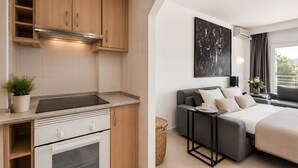 A compact kitchen with modern appliances, a dining area with a grey sofa and a small table, and a bedroom with a bed and a large window. - Sol Wave House with Sea Views, Wi-Fi and Air Conditioning (Magaluf)
