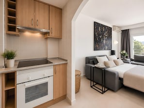 A compact kitchen with modern appliances, a dining area with a grey sofa and a small table, and a bedroom with a bed and a large window. - Sol Wave House with Sea Views, Wi-Fi and Air Conditioning (Magaluf)