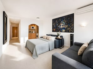 A modern hotel room with a bed, a sofa, a kitchen area, and a large abstract painting on the wall. - Sol Wave House with Sea Views, Wi-Fi and Air Conditioning (Magaluf)