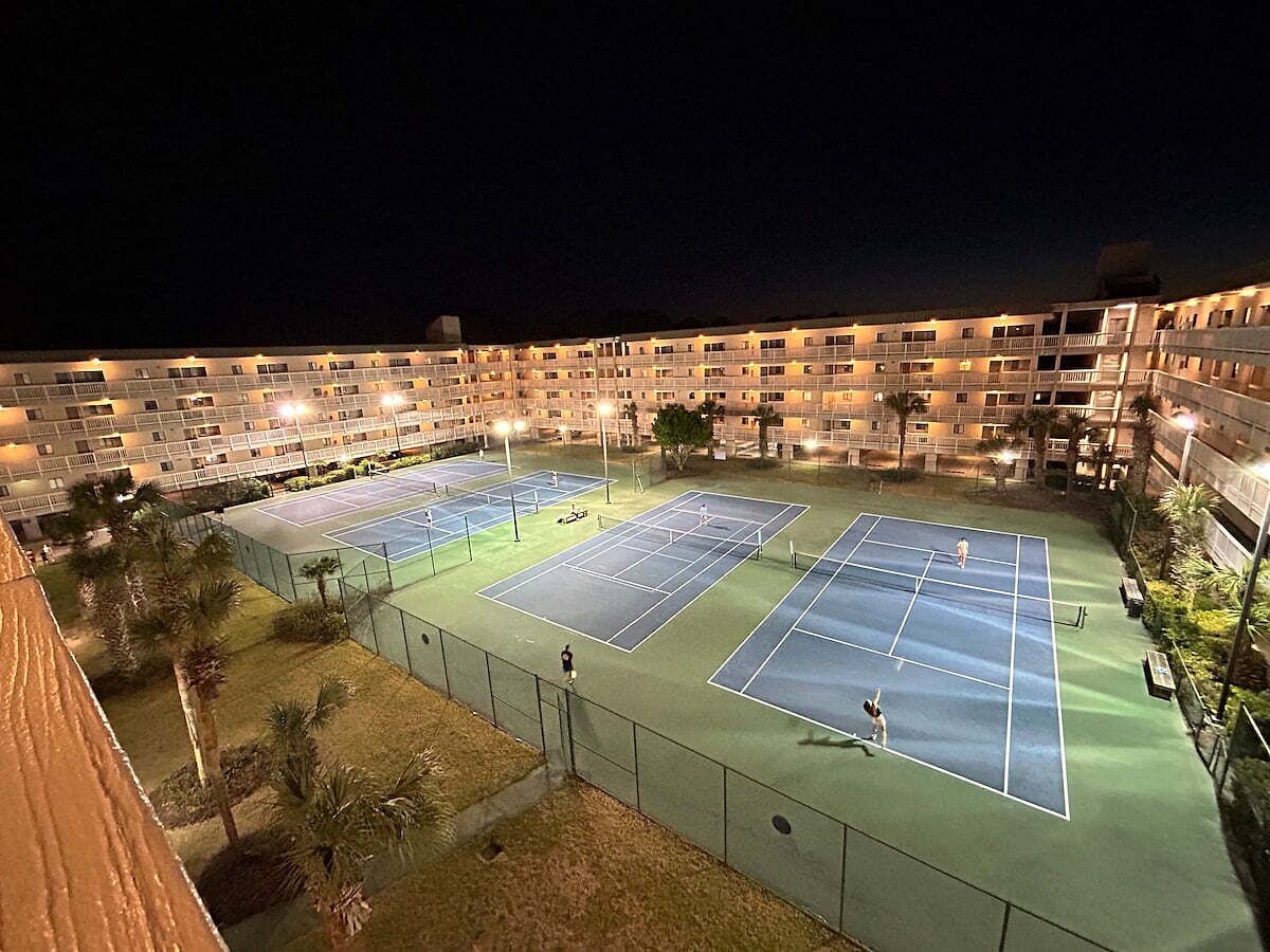 Un hôtel à plusieurs étages doté de nombreux courts de tennis, chacun étant entouré d’une clôture et éclairé par un système d’éclairage artificiel.