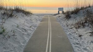 Un sendero que lleva a una playa con dunas de arena y un cartel.