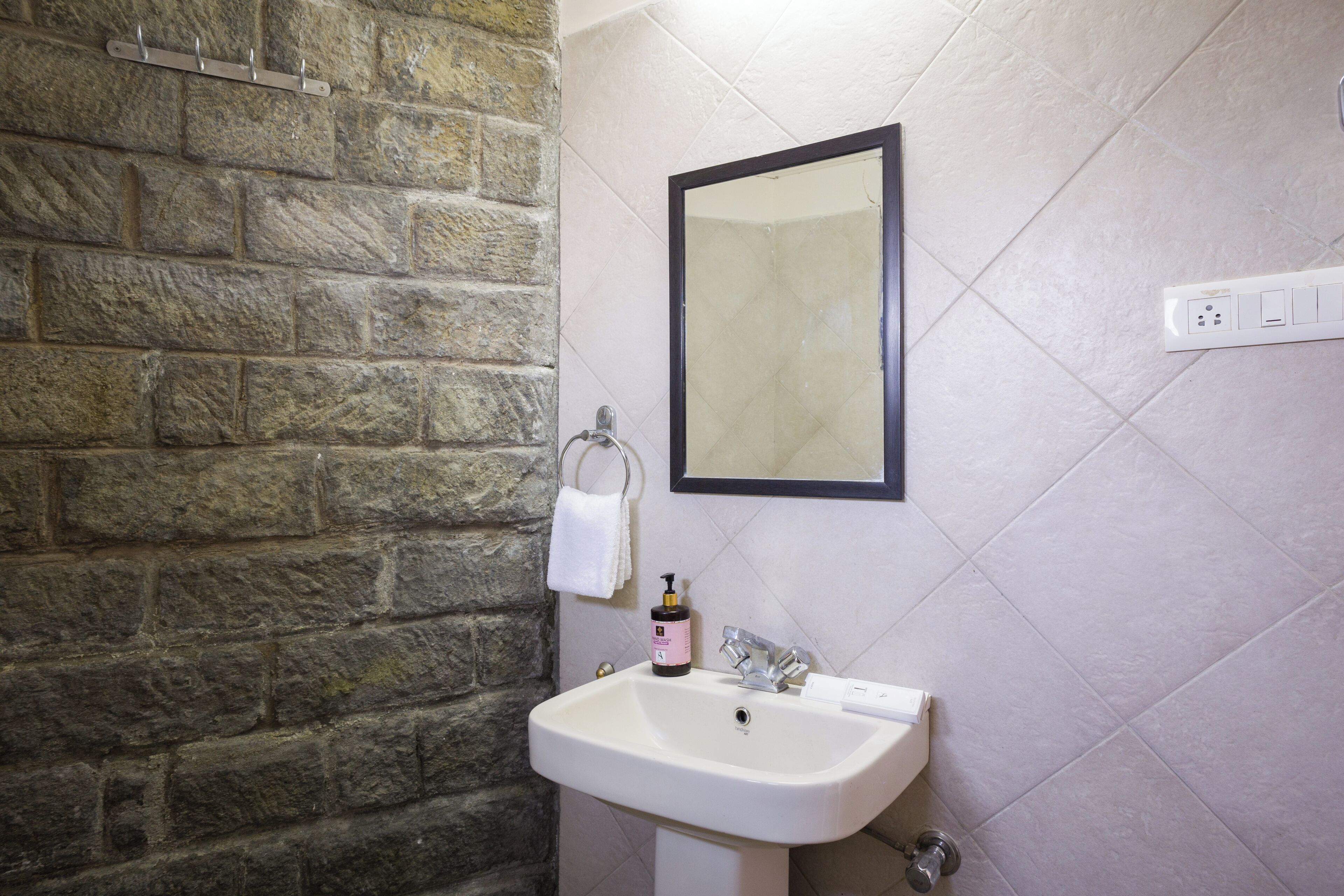 Une salle de bain avec un mur en pierre, un lavabo blanc, un miroir et un porte-serviettes.