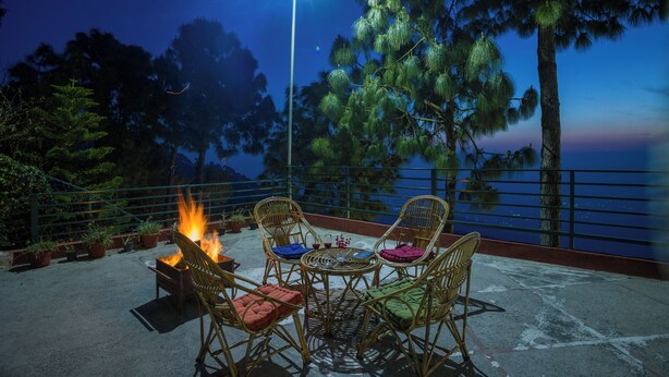 Eine Terrasse mit Korbstühlen, einem kleinen Tisch und einem Feuer.
