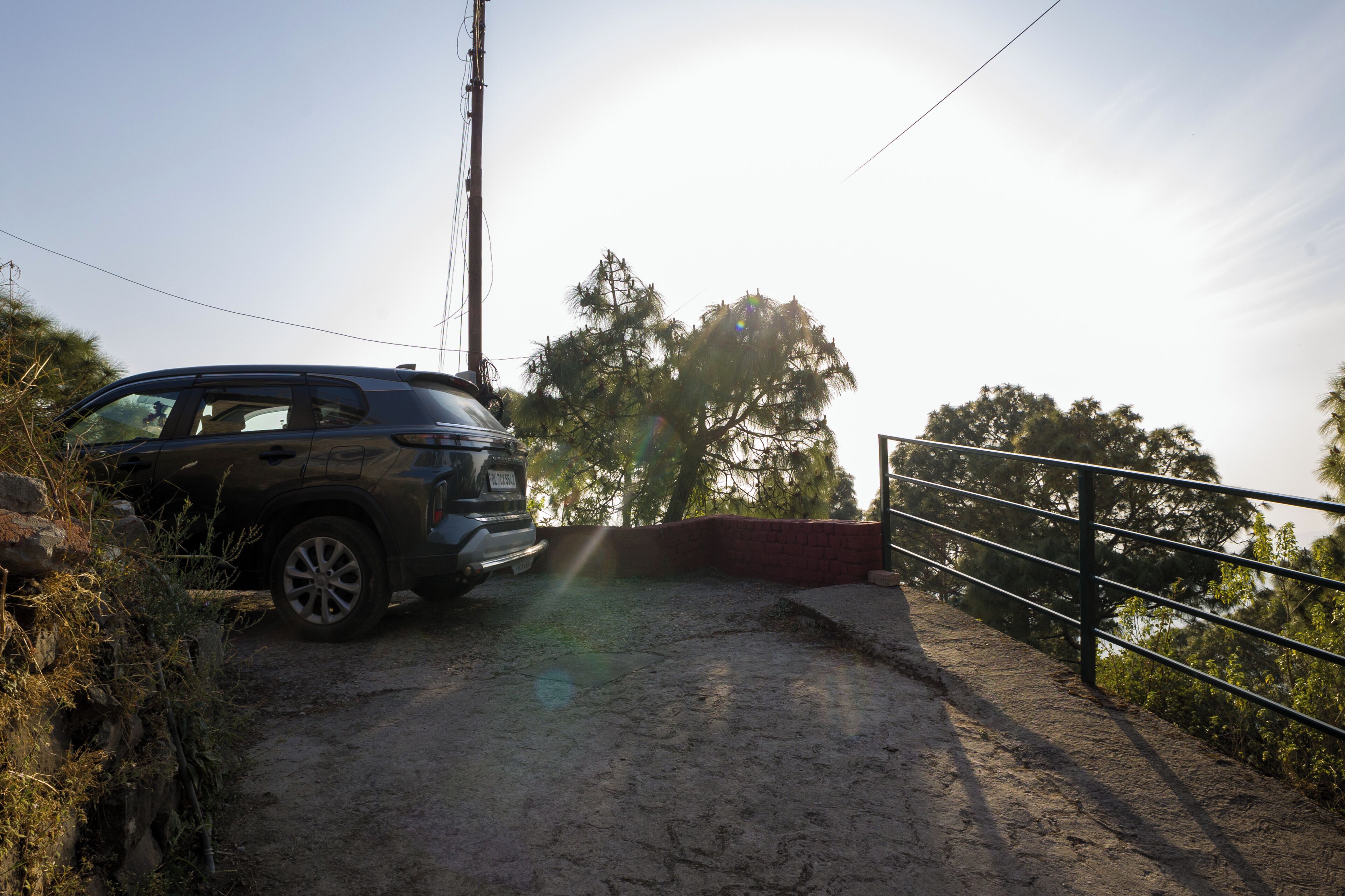A vehicle parked on a dirt path with a metal railing and trees in the background.